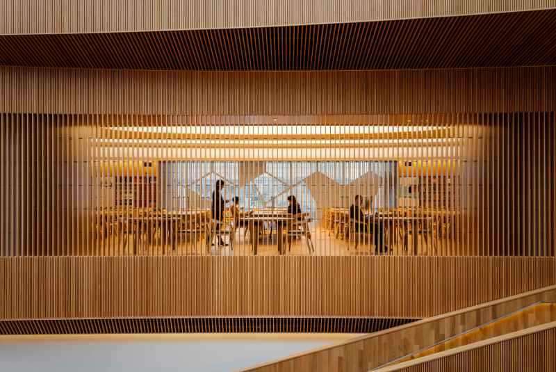 Interior view of a modern wooden space with vertical slats, featuring tables and people engaged in discussions.